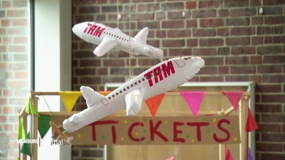 Aufblasbare Flugzeuge hängen vor einem selbst gebasteltem Ticketschalter. © Screenshot 
